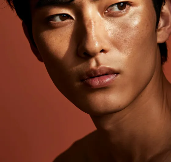 Close-up portrait of a young man with smooth skin looking to the side against a plain brown background.